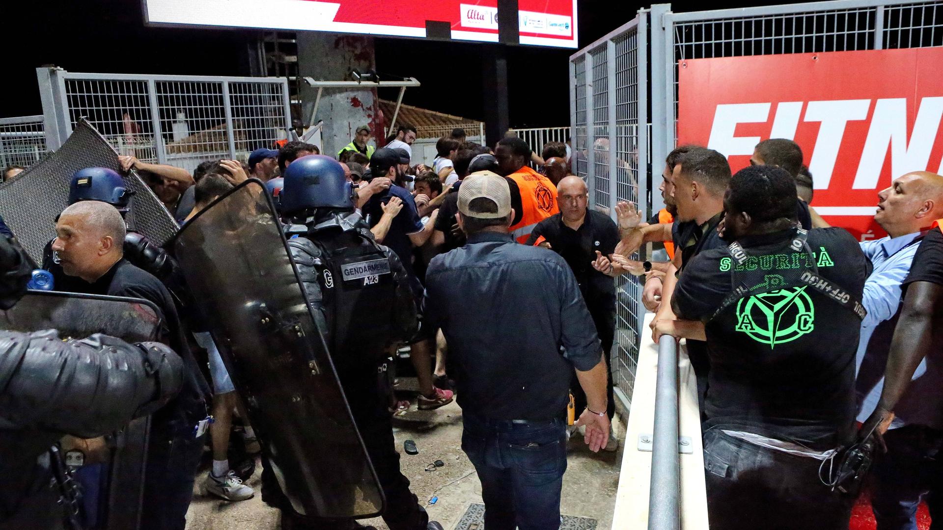 Polizisten in Schutzausrüstung drängen randalierende Fußballfans zurück. Polizisten in Schutzausrüstung drängen randalierende Fußballfans zurück.