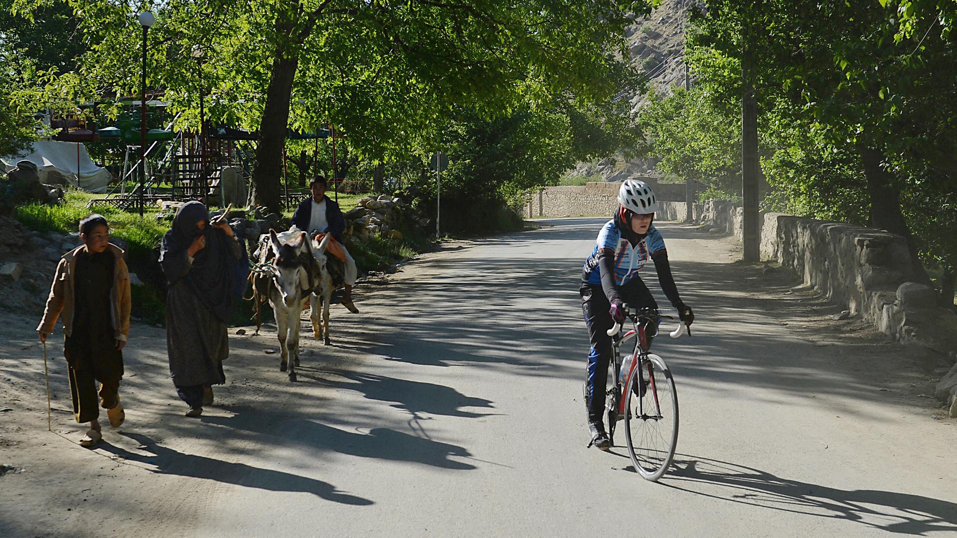 Eine afghanische Frau auf ihrem Rennrad wird von den Menschen am Wegesrand beäugt. 
