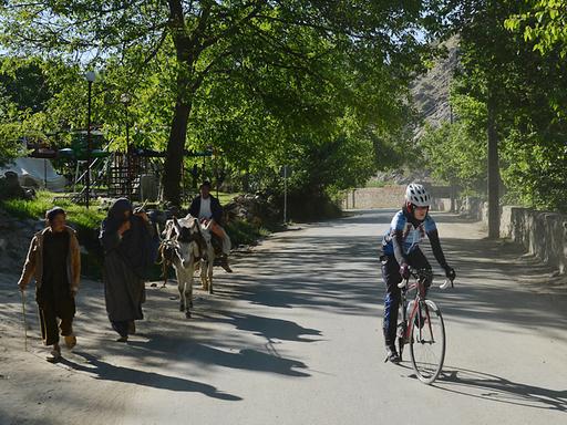 Eine afghanische Frau auf ihrem Rennrad wird von den Menschen am Wegesrand beäugt. 