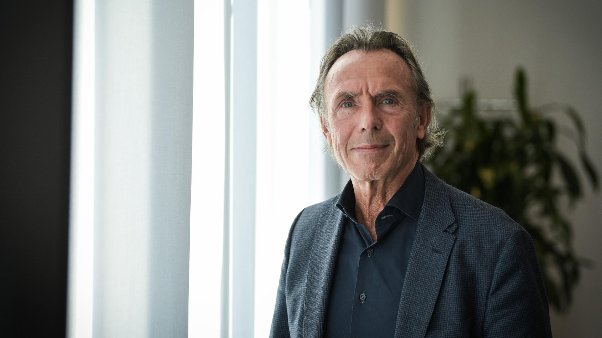 Thomas Druyen trägt ein dunkles Hemd, ein dunkles Sakko und steht vor einem mit Gardinen verhangenen Fenster. Thomas Druyen trägt ein dunkles Hemd, ein dunkles Sakko und steht vor einem mit Gardinen verhangenen Fenster.