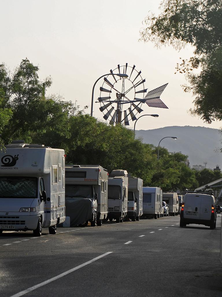 Blick in eine von Wohnmobilen gesäumte Straße. Am Ende der Straße ist zwischen den Bäumen ein Windrad zu sehen.