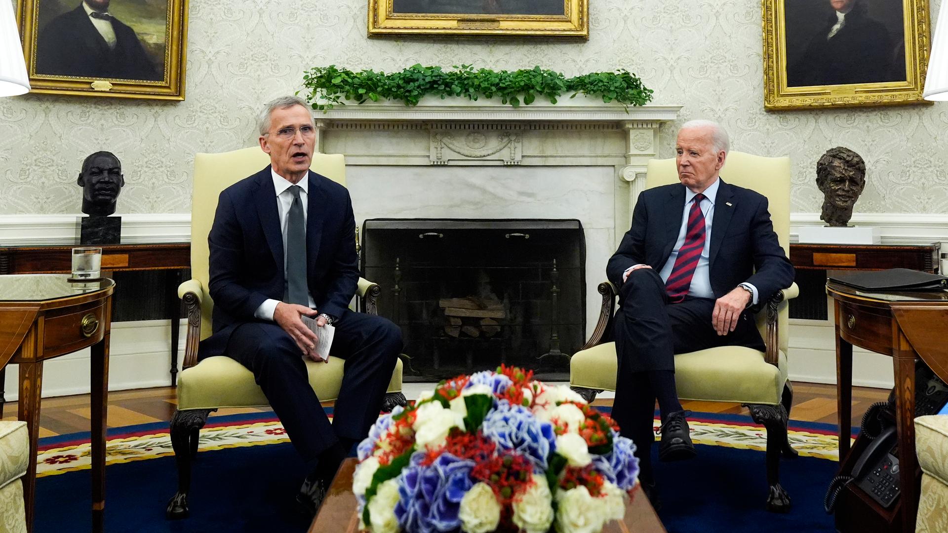 Joe Biden und Jens Stoltenberg sitzen im Oval Office im Weißen Haus auf zwei Stühlen nebeneinander. In der Mitte hinter ihnen ist ein offener Kamin zu sehen. 