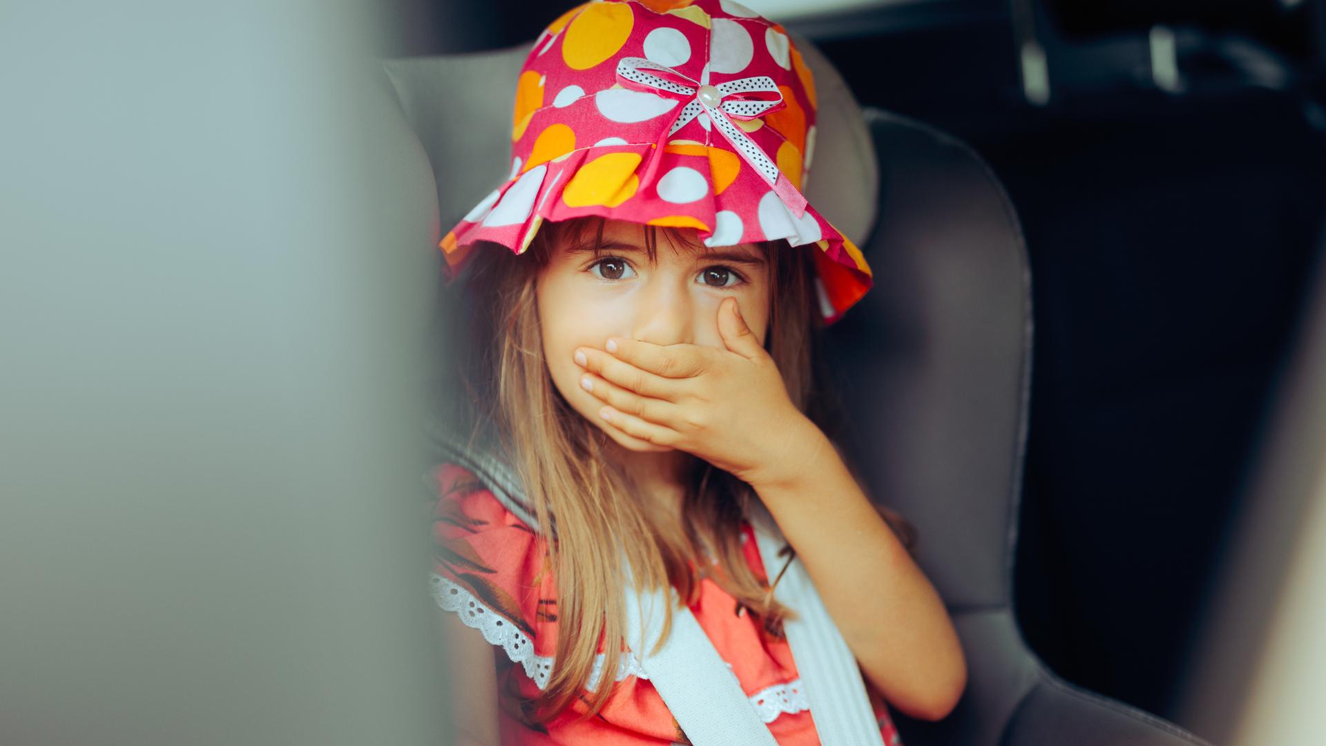 Ein Mädchen bei der Autofahrt hält sich die Hand vor den Mund