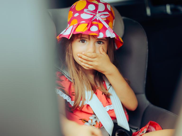 Ein Mädchen bei der Autofahrt hält sich die Hand vor den Mund