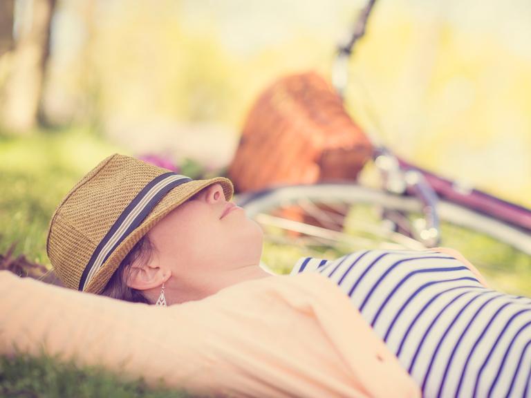 Eine erwachsenes Frau ruht sich im New Yorker Central Park aus. Im Hintergrund ist ein Fahrrad und eine Art Picknickkorb zu erkennen.