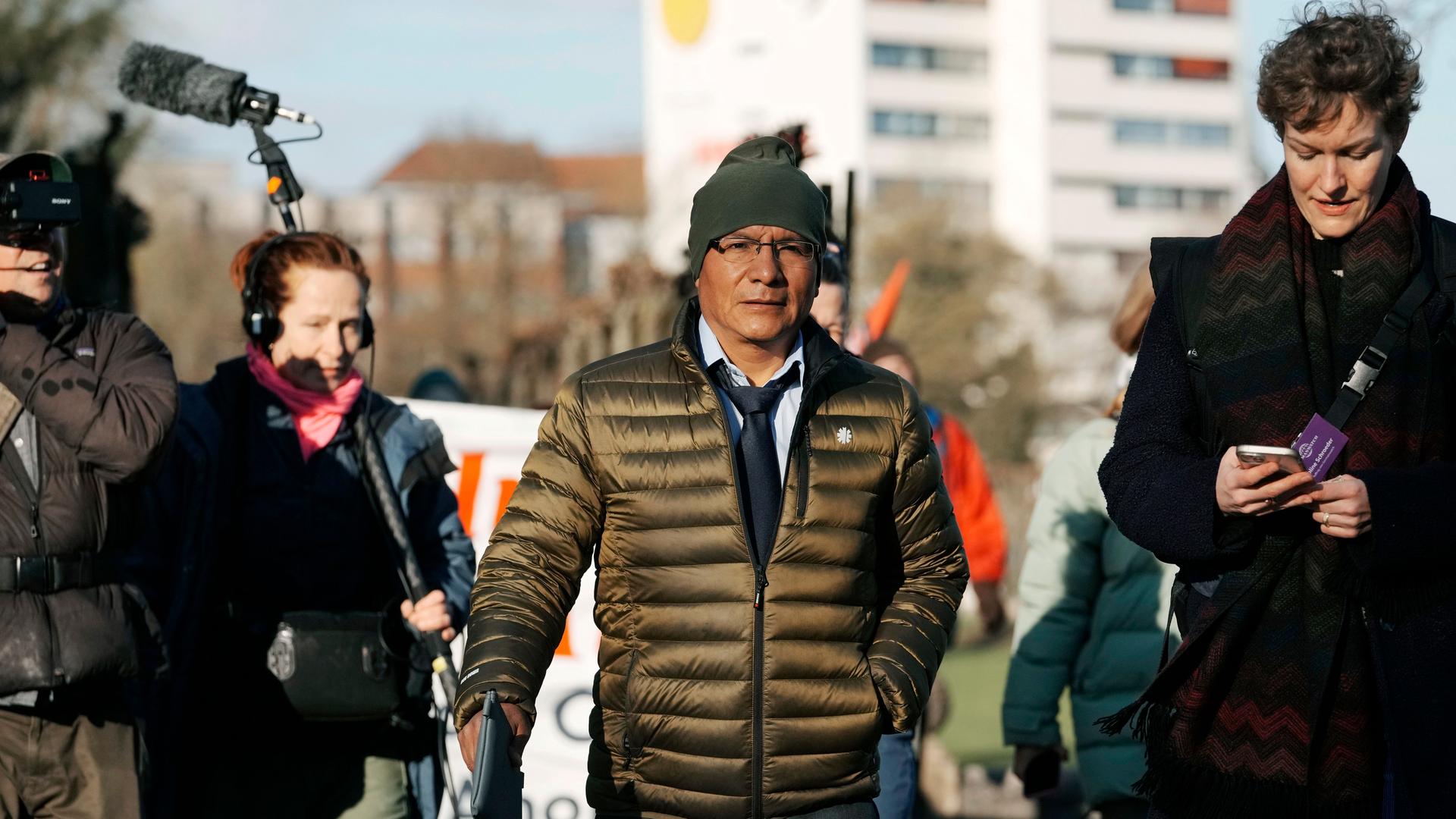 Der peruanische Bauer Luciano Lliuya geht neben einigen Journalisten auf einer Straße. Er trägt eine Mütze und eine Jacke.  