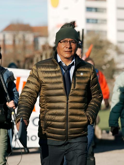 Der peruanische Bauer Luciano Lliuya geht neben einigen Journalisten auf einer Straße. Er trägt eine Mütze und eine Jacke.  
