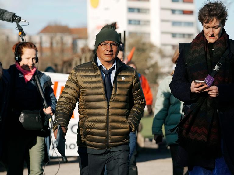 Der peruanische Bauer Luciano Lliuya geht neben einigen Journalisten auf einer Straße. Er trägt eine Mütze und eine Jacke.  