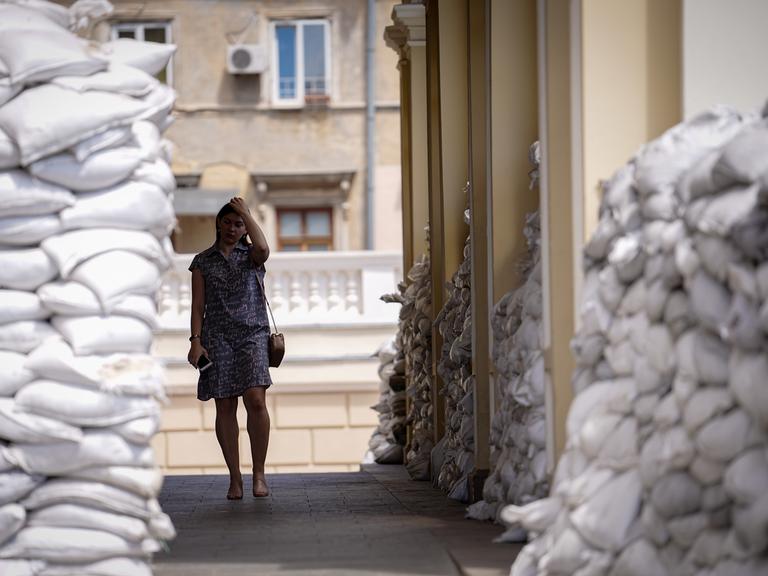 Eine Frau in einem Sommerkleid geht durch einen Wall aus Sandsäcken vor der Oper der ukrainischen Hafenstadt Odessa.