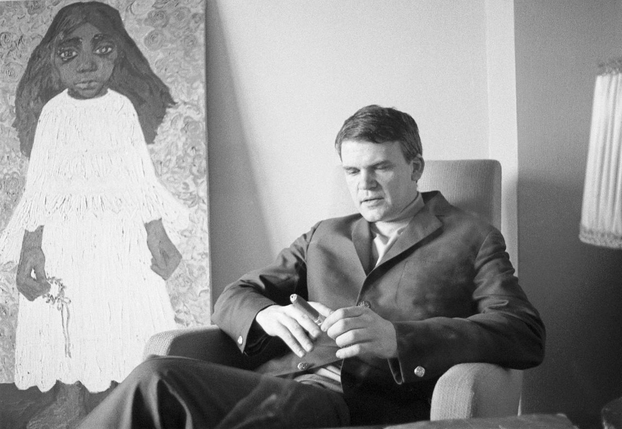 Der tschechische Schriftsteller Milan Kundera sitzt mit einer Zigarre in der Hand in einem Sessel. Dahinter ist eine Malerei zu sehen. Das schwarz-weiße Foto wurde im Mai 1968 aufgenommen.