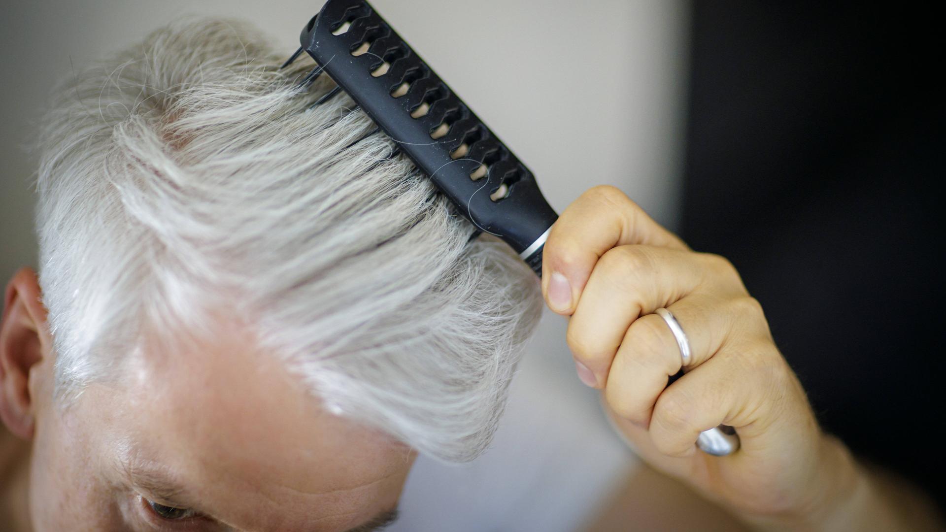 Ein Mann kämmt mit einer Bürste seine grauen Haare. 