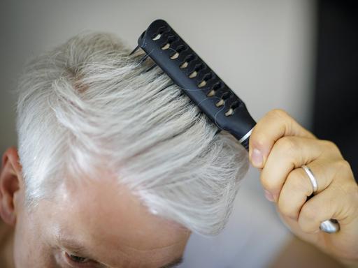 Ein Mann kämmt mit einer Bürste seine grauen Haare. 