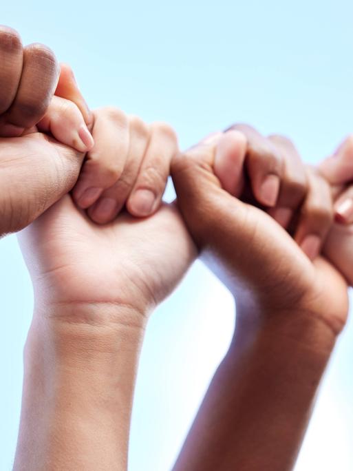 Zwei Paar Hände bilden quasi eine Kette. Die eine Faust hält den Daumen einer anderen Hand.
