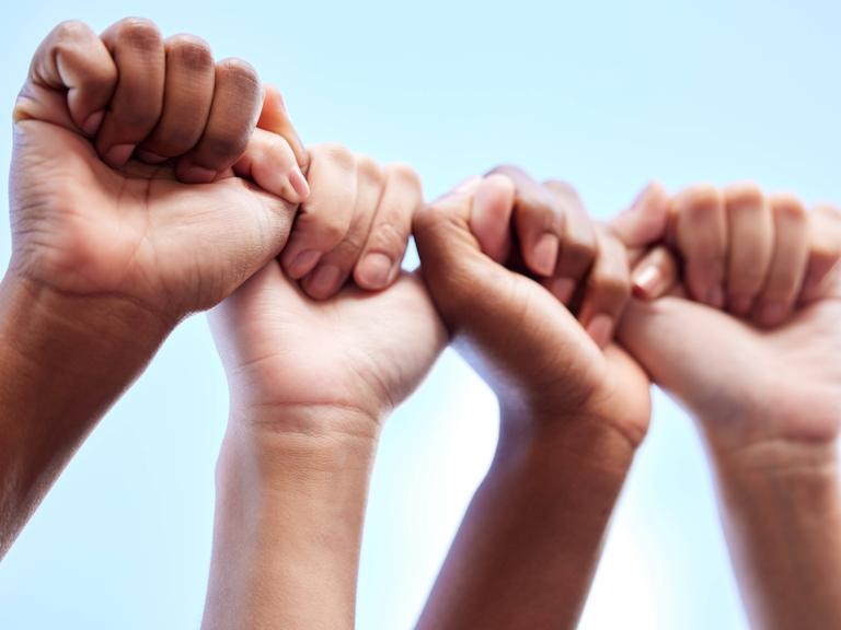 Zwei Paar Hände bilden quasi eine Kette. Die eine Faust hält den Daumen einer anderen Hand.