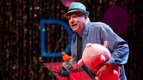 Rosa von Praunheim spricht mit Hut auf dem Kopf bei der Verleihung der 39. Teddy Awards am Rande der Berlinale und hält dabei ein rosa Stoffschwein im Arm. Rosa von Praunheim spricht mit Hut auf dem Kopf bei der Verleihung der 39. Teddy Awards am Rande der Berlinale und hält dabei ein rosa Stoffschwein im Arm.