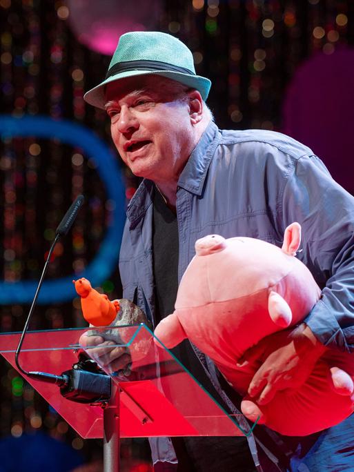 Rosa von Praunheim spricht mit Hut auf dem Kopf bei der Verleihung der 39. Teddy Awards am Rande der Berlinale und hält dabei ein rosa Stoffschwein im Arm.