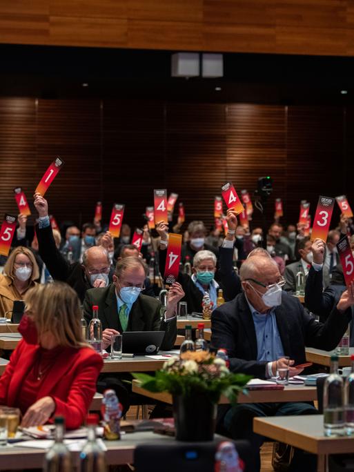 Bei der jährlichen Versammlung des DOSB stimmen die Teilnehmer:innen per hochgehaltener Abstimmungskarte ab.