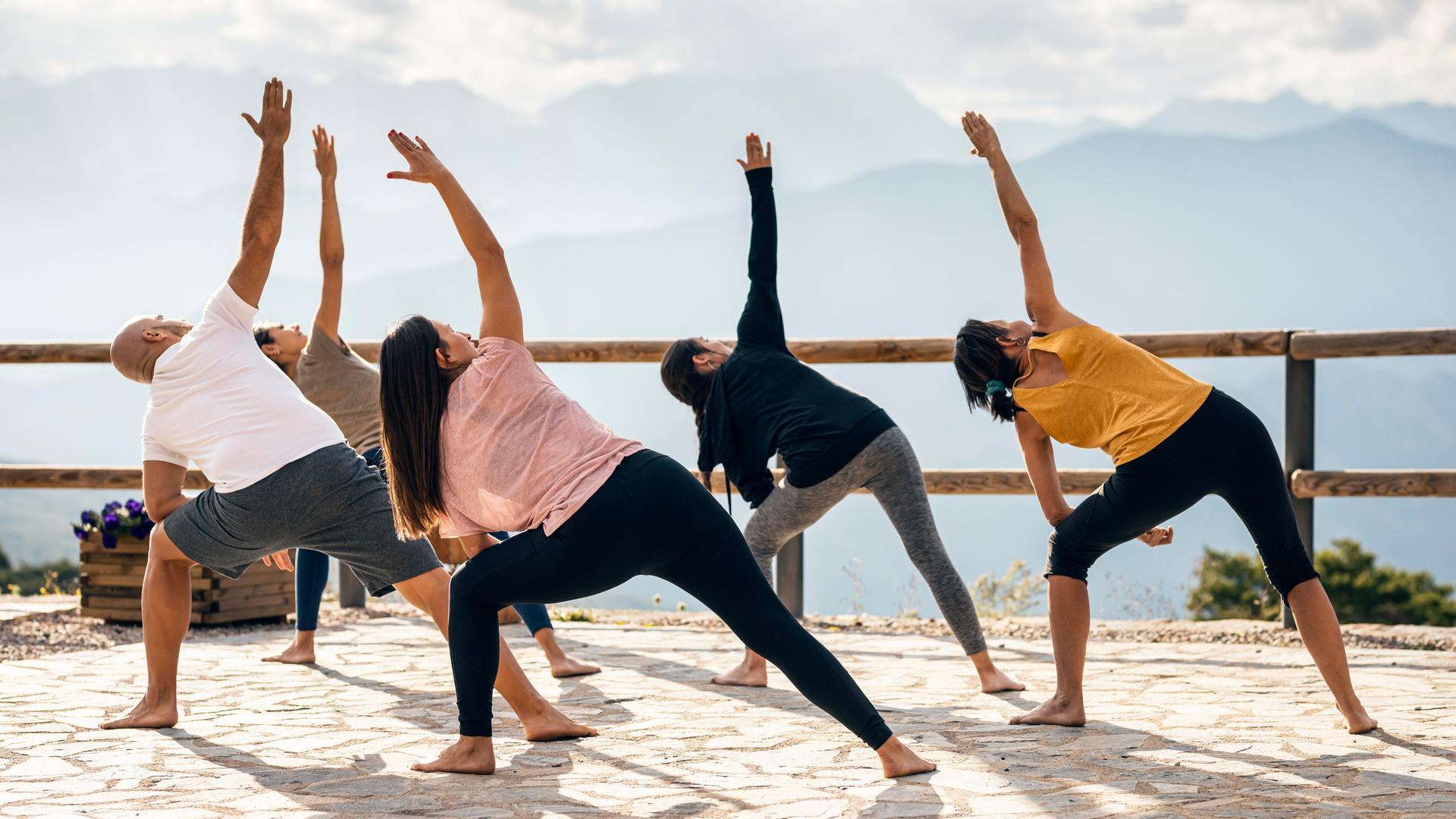 Fünf Menschen machen an einem sonnigen Tag Yoga draußen