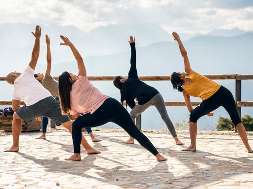 Fünf Menschen machen an einem sonnigen Tag Yoga draußen