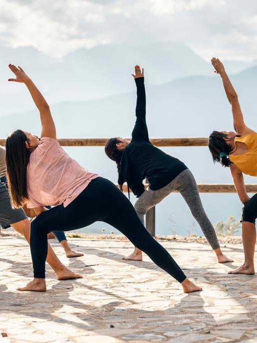 Fünf Menschen machen an einem sonnigen Tag Yoga draußen