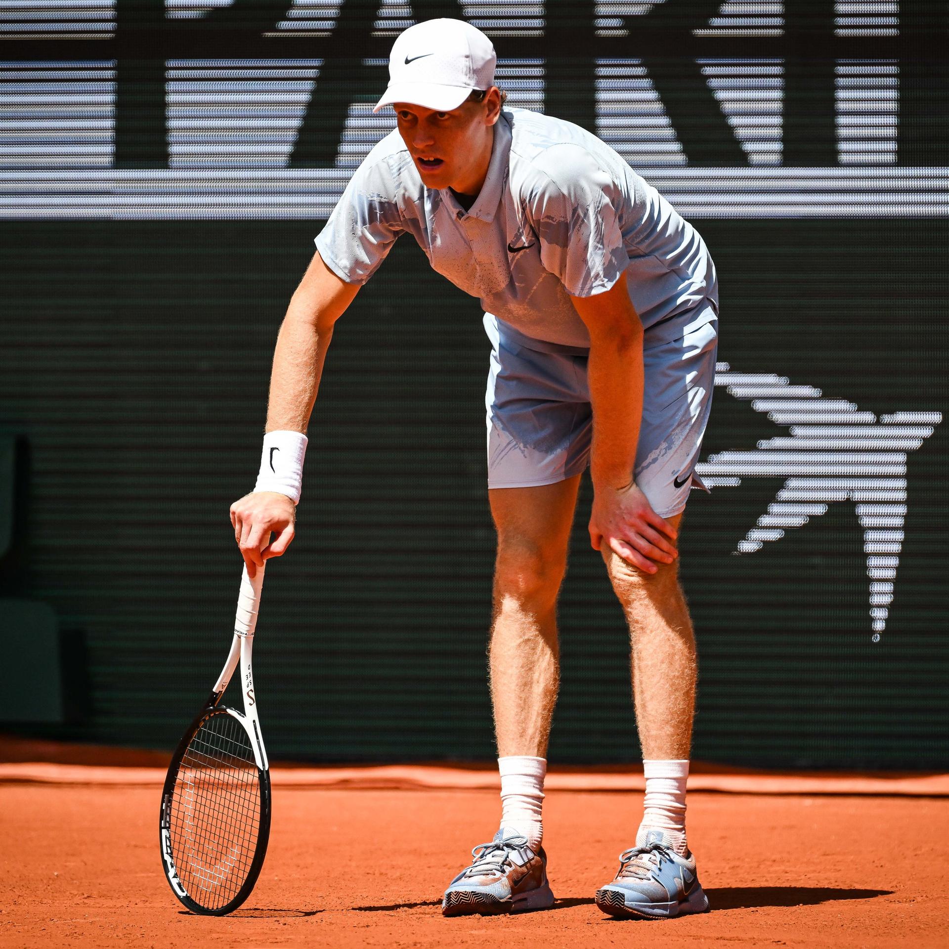 French Open: Jannik Sinner hatte wegen der Hitze in Paris große körperliche Probleme. Er steht auf dem Platz, beugt sich nach vorne und stützt sich mit dem Tennisschläger am Boden ab.