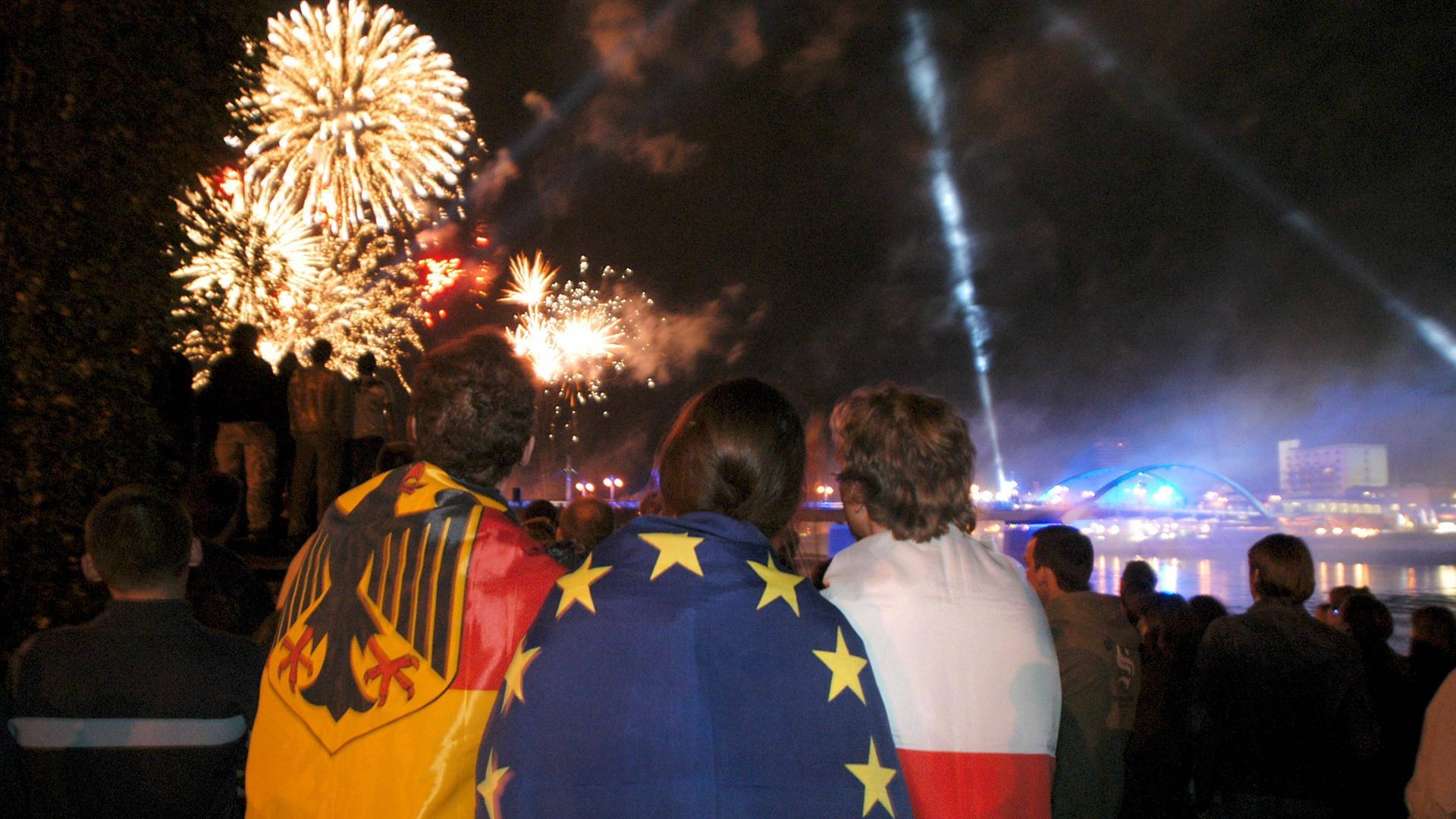 Jugendliche aus der polnischen Grenzstadt Slubice haben sich Fahnen von Europa, Deutschland und Polen umgehängt und beobachten ein Feuerwerk.