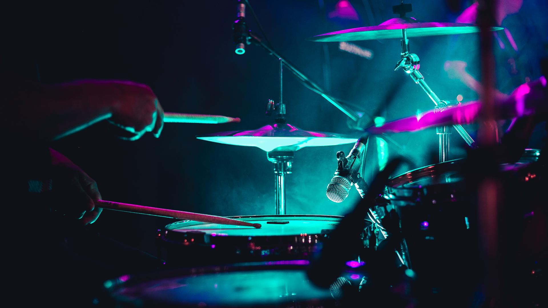 Nahaufnahme eines Drumsets in neonfarbener Bühnenbeleuchtung.