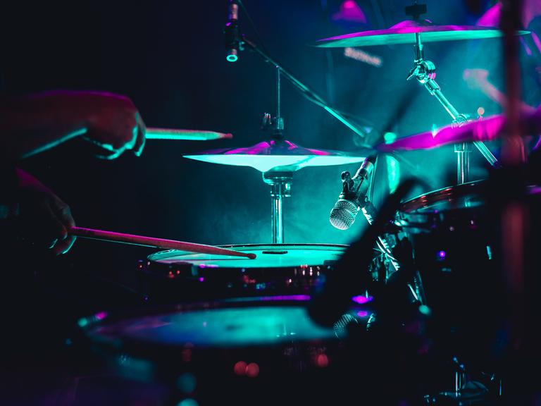Nahaufnahme eines Drumsets in neonfarbener Bühnenbeleuchtung.