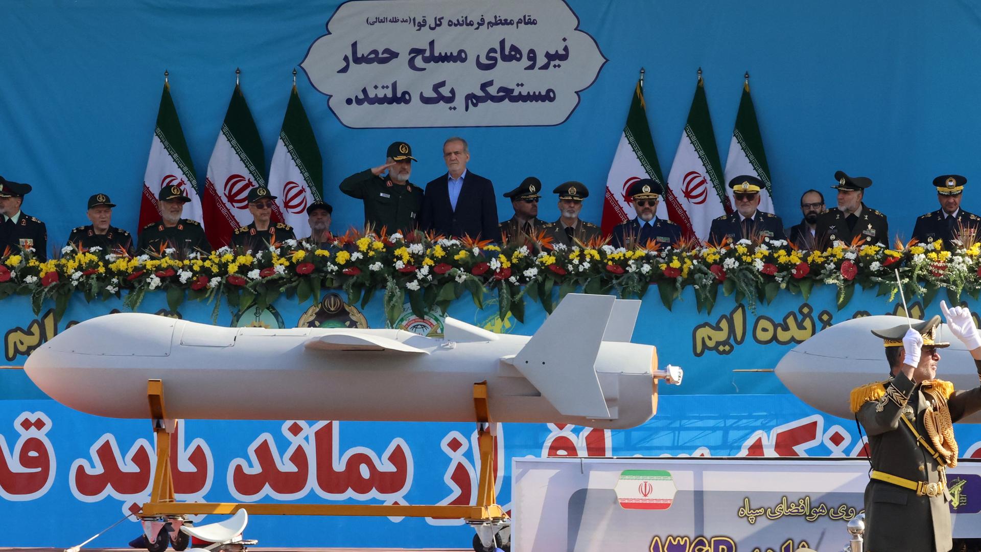 Irans Präsident Peseschkian steht zusammen mit Militärs auf einer Bühne und nimmt eine Militärparade ab, bei der die neueste Version der Shahed-Drohne gezeigt wird. Irans Präsident Peseschkian steht zusammen mit Militärs auf einer Bühne und nimmt eine Militärparade ab, bei der die neueste Version der Shahed-Drohne gezeigt wird.