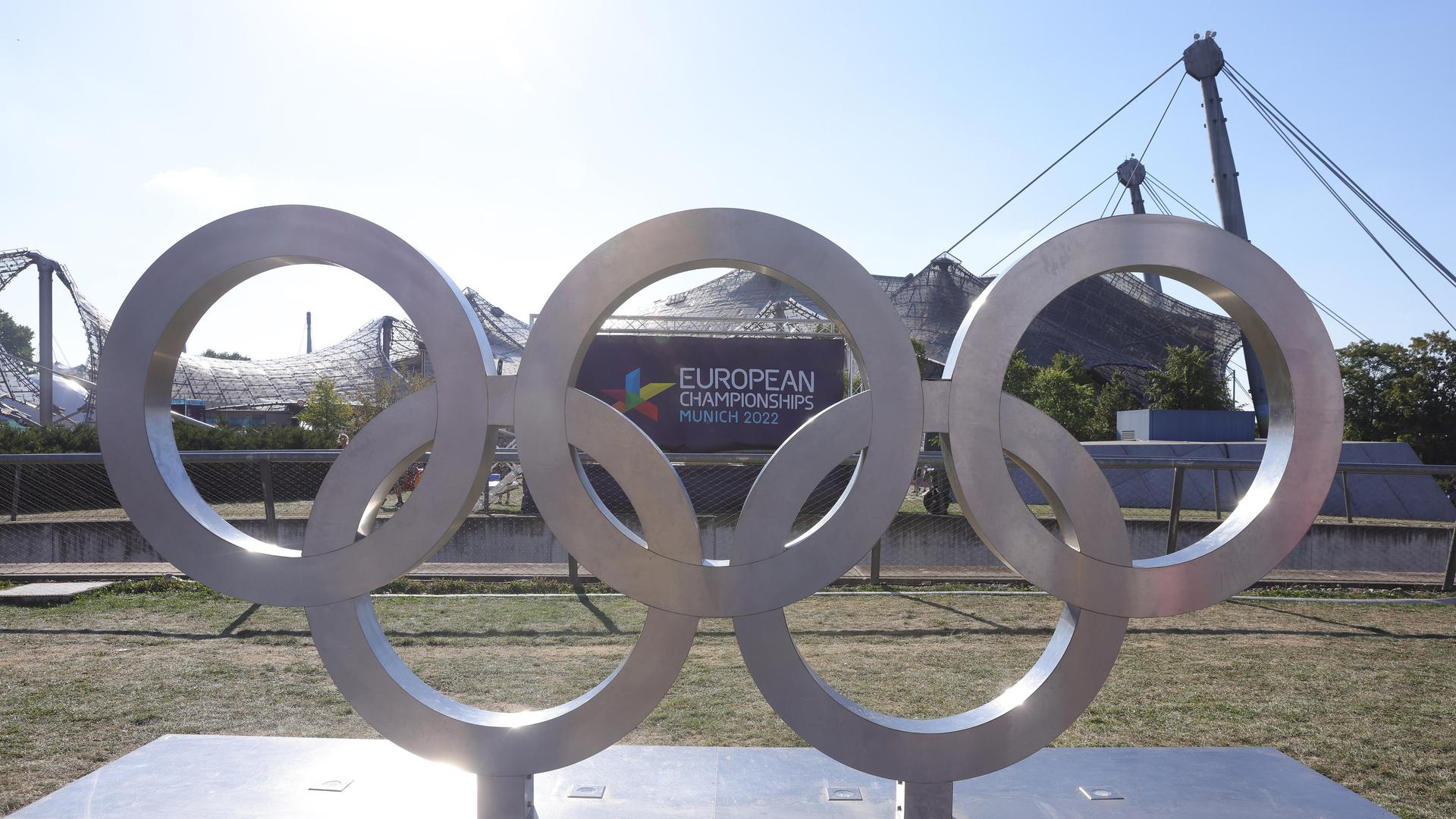Olympische Ringe stehenin München vor dem Plakat der European Championships
