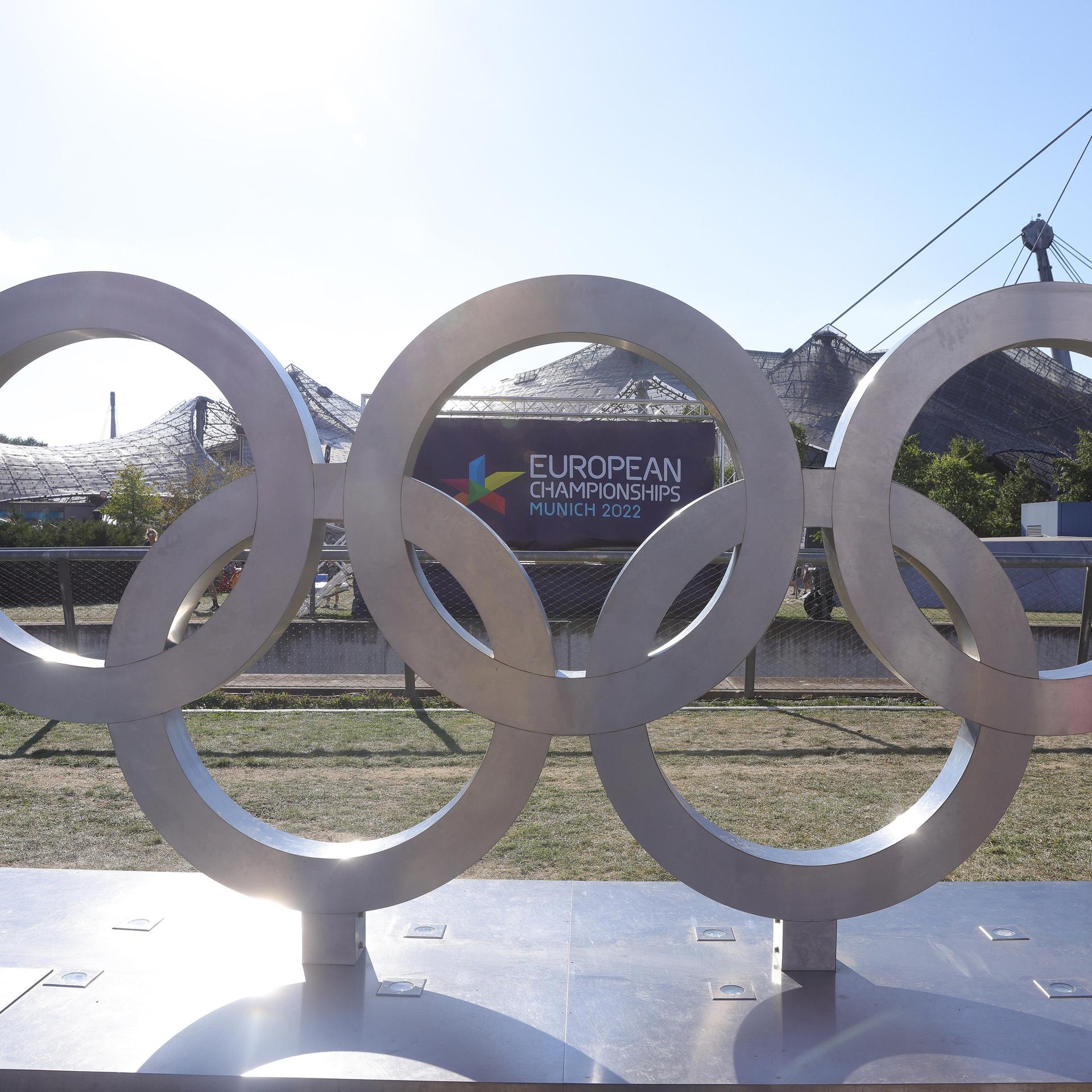 Olympische Ringe stehenin München vor dem Plakat der European Championships