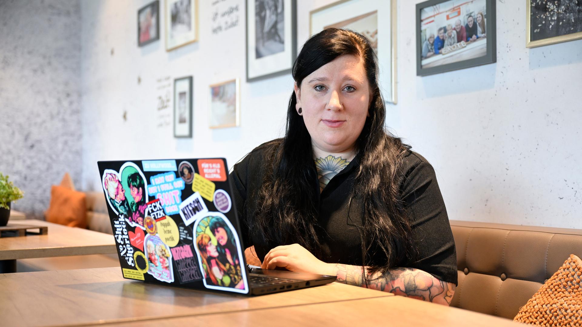 Die Autorin Lena Schätte beim Schreiben in einem Cafe. Vor ihr ein Laptop mit zahlreichen Aufklebern.