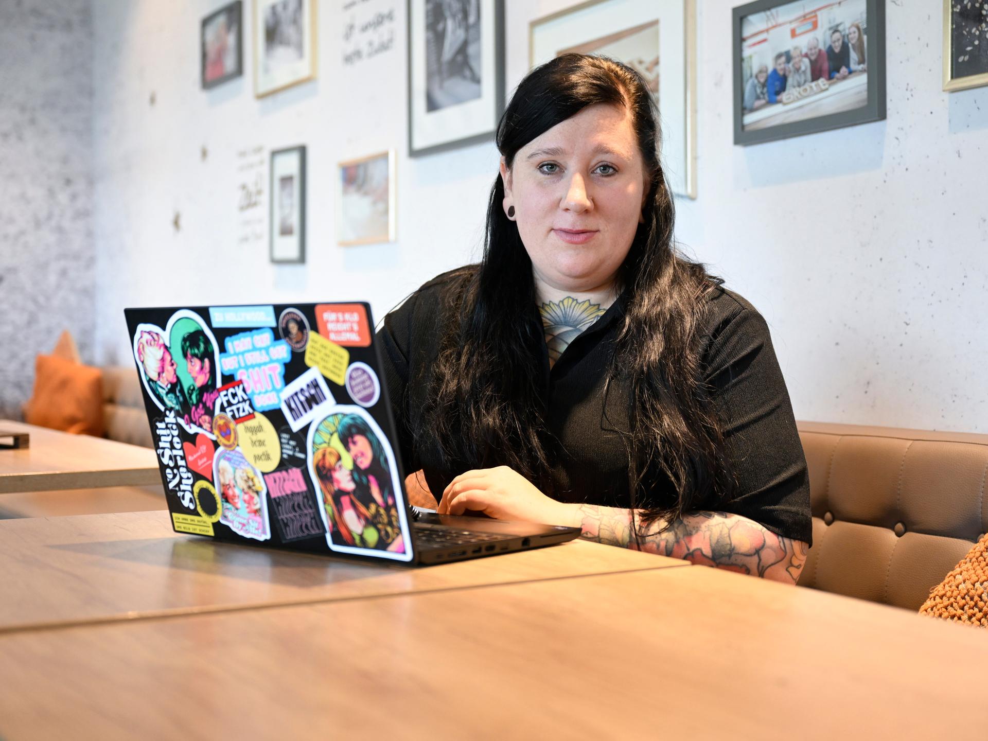 Die Autorin Lena Schätte beim Schreiben in einem Cafe. Vor ihr ein Laptop mit zahlreichen Aufklebern.