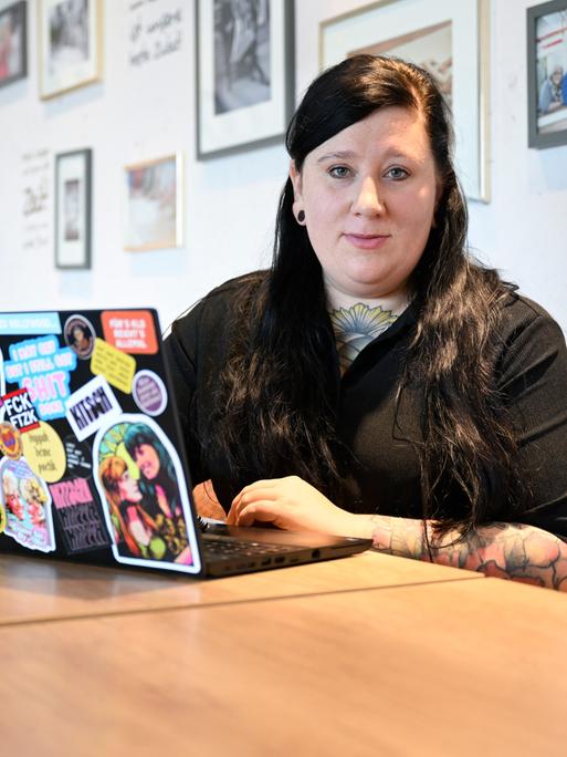 Die Autorin Lena Schätte beim Schreiben in einem Cafe. Vor ihr ein Laptop mit zahlreichen Aufklebern.
