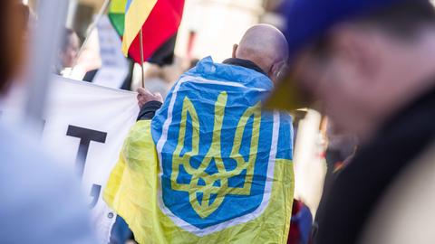 Ein Mann hat sich auf einer Demo die Flagge der Ukraine über die Schultern gehängt.