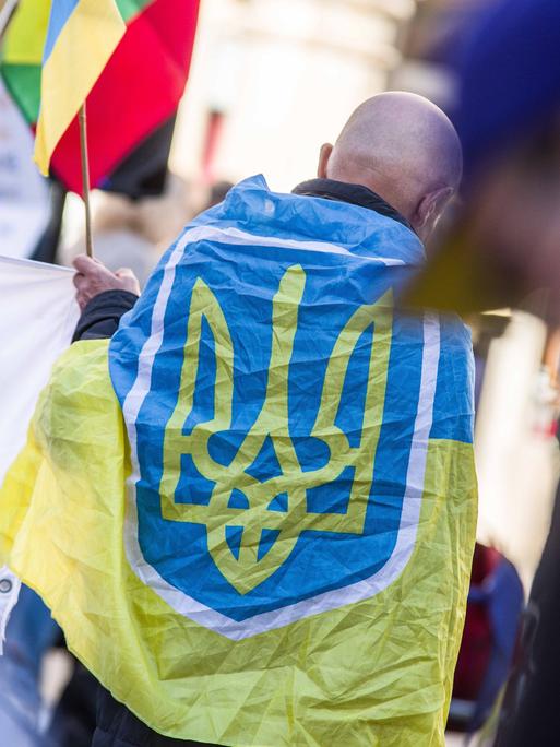 Ein Mann hat sich auf einer Demo die Flagge der Ukraine über die Schultern gehängt.