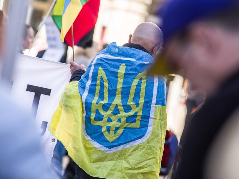 Ein Mann hat sich auf einer Demo die Flagge der Ukraine über die Schultern gehängt.