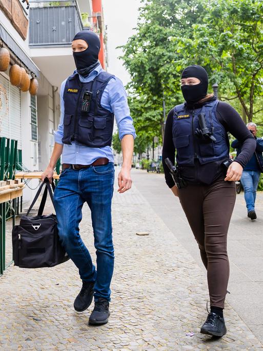 Zwei Polizisten gehen bei einer Hausdurchsuchung in Berlin-Kreuzberg zu einem Gebäude. 