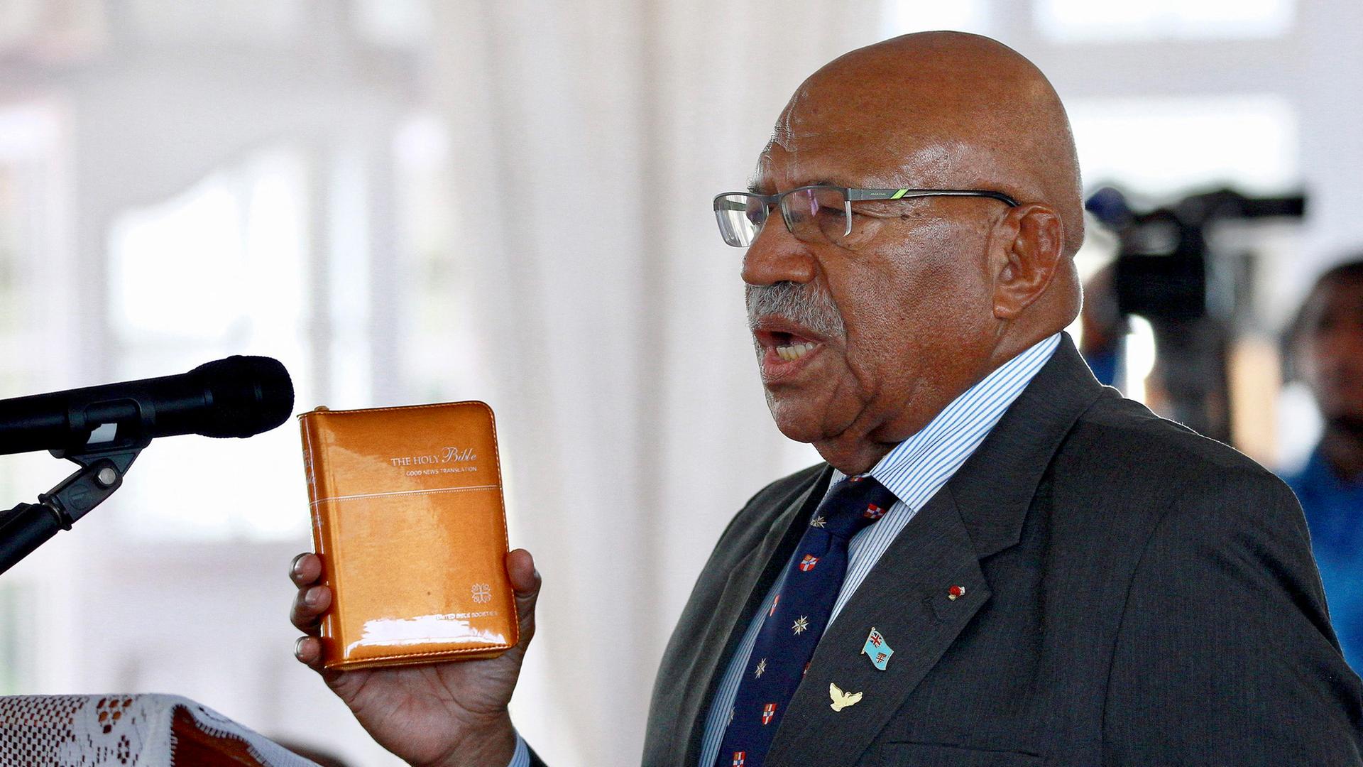 Sitiveni Rabuka ist als Premierminister der Fidschi-Inseln vereidigt worden. Er hält ein Buch in der Hand und spricht in ein Mikrofon.