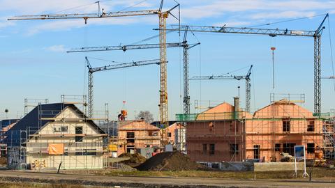 In einem Neubaugebiet stehen viele Baukräne vor Wohnhäuser im Rohbau, als Symbolbild für Wohnungsbau.