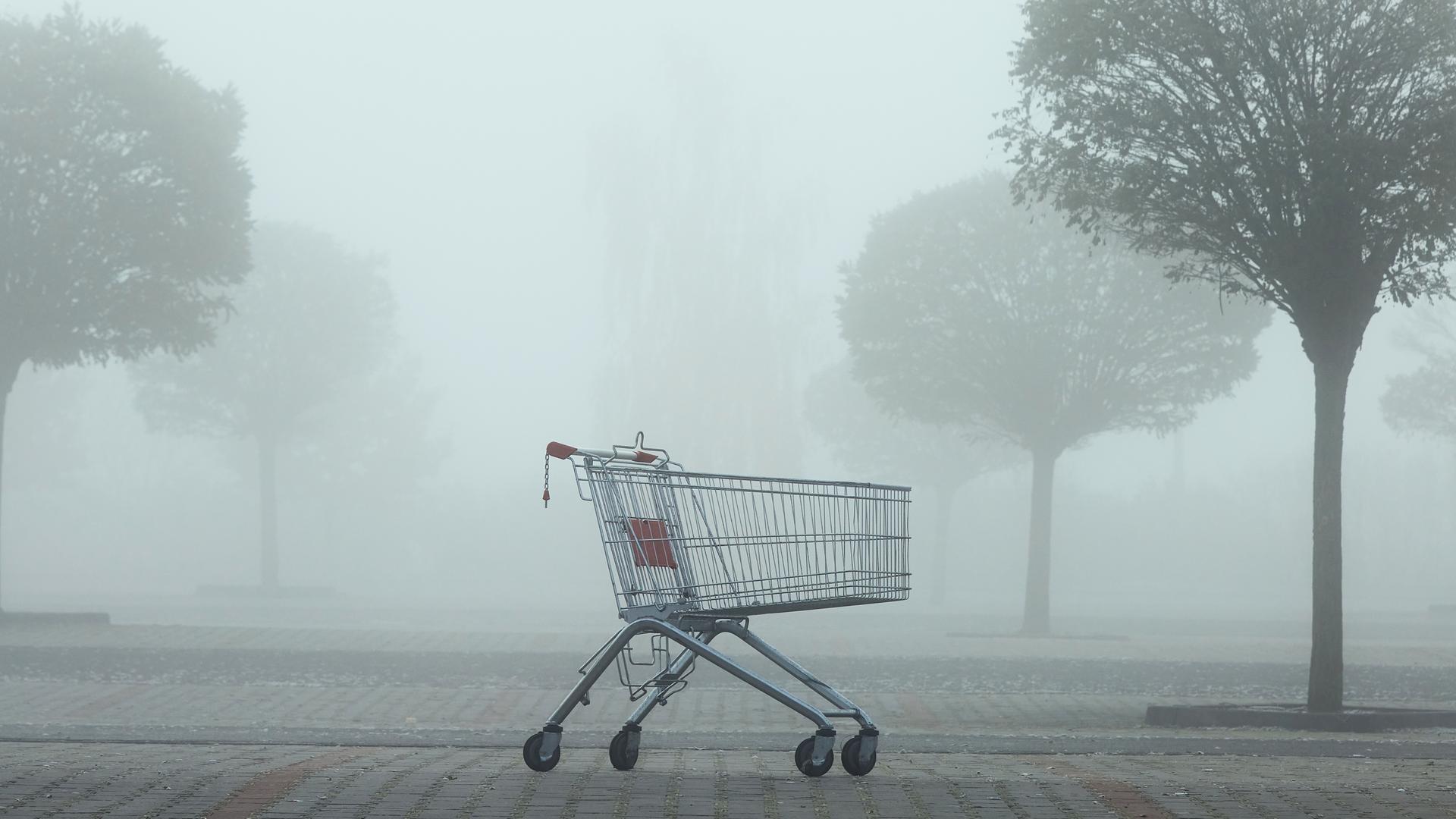 Ein leerer Einkaufswagen steht einsam auf einem nebligen Parkplatz.