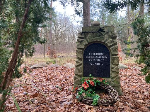 Im Wald steht ein Gedenkstein mit der Aufschrift "Friedhof der ehemaligen Ortschaft Wunder". Davor wurde ein Grabkranz abgelegt.