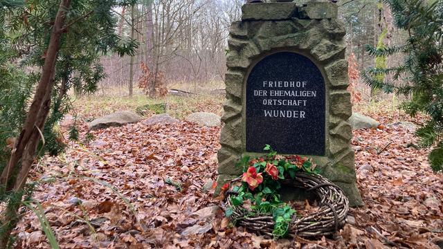 Im Wald steht ein Gedenkstein mit der Aufschrift "Friedhof der ehemaligen Ortschaft Wunder". Davor wurde ein Grabkranz abgelegt.