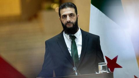 Ahmed al-Scharaa steht an einem Rederpult. Er trägt Hemd, Anzug und Krawatte und spricht in ein Mikrofon.