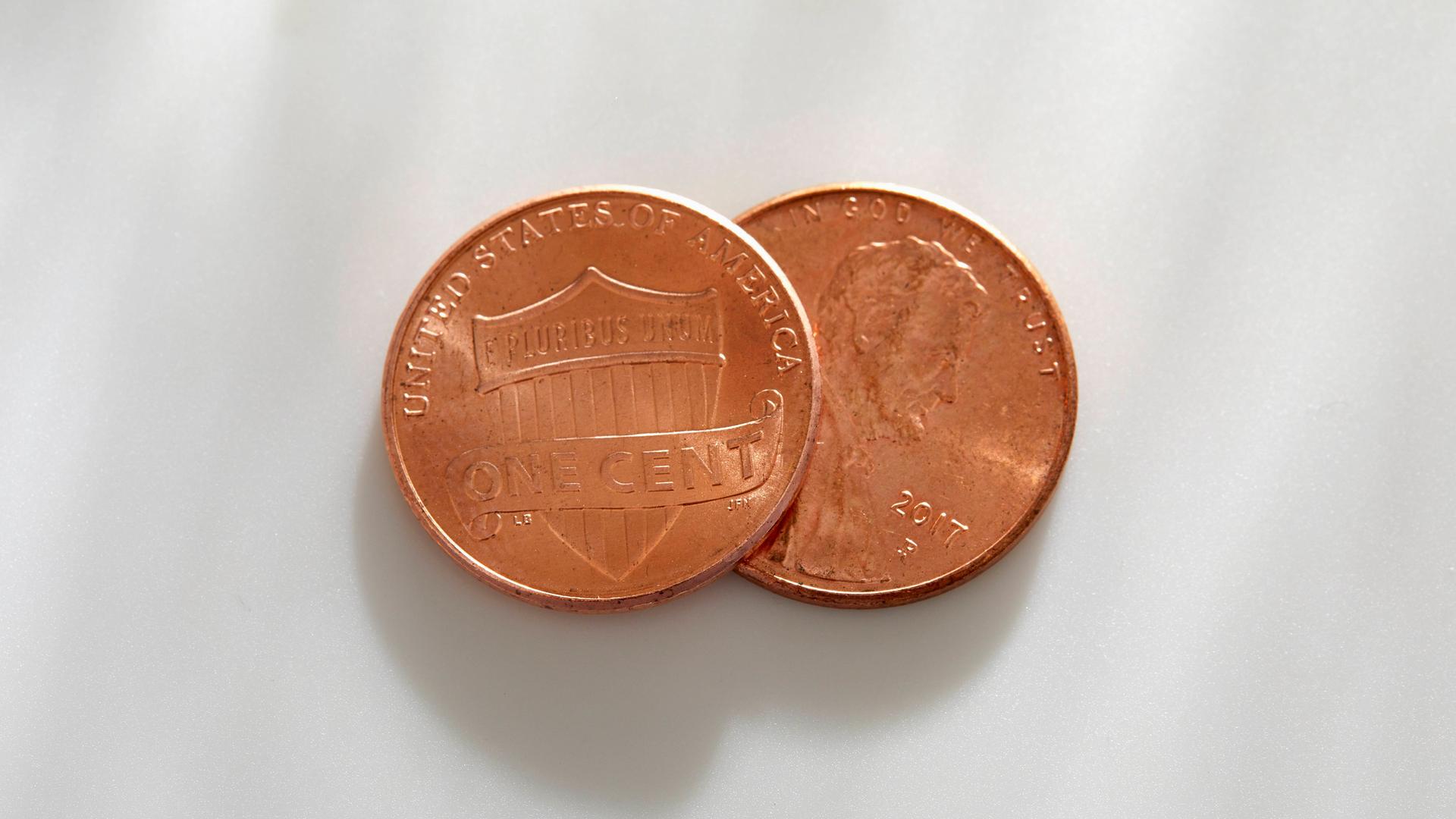 Zwei kupferfarbene Münzen liegen auf weißem Untergrund. Zwei kupferfarbene Münzen liegen auf weißem Untergrund.