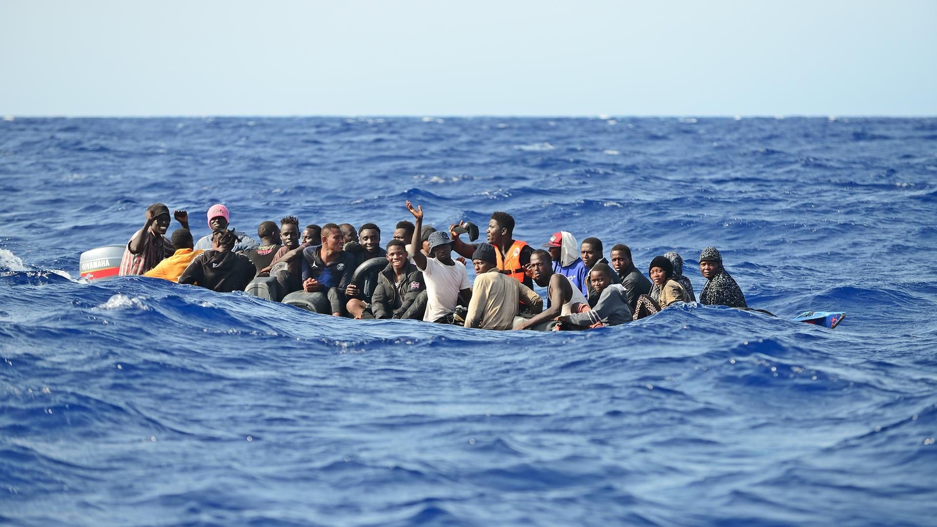 Etwa 30 Geflüchtete sitzen in einem Holzboot, sie versuchen bei hohem Wellengang die gefährliche Überfahrt nach Italien. 