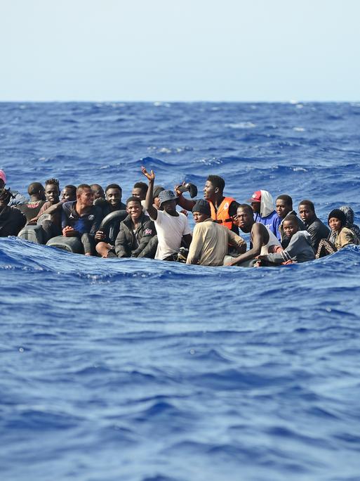 Etwa 30 Geflüchtete sitzen in einem Holzboot, sie versuchen bei hohem Wellengang die gefährliche Überfahrt nach Italien. 