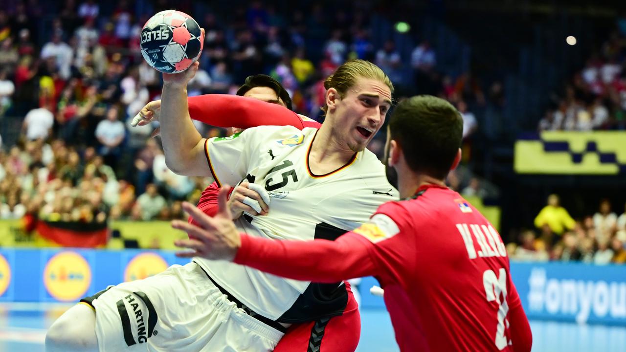 Juri Knorr versucht sich gegen einen anderen Handballspieler durchzusetzen. Er trägt ein weißes Trikot und hält den Ball in seiner Hand.
