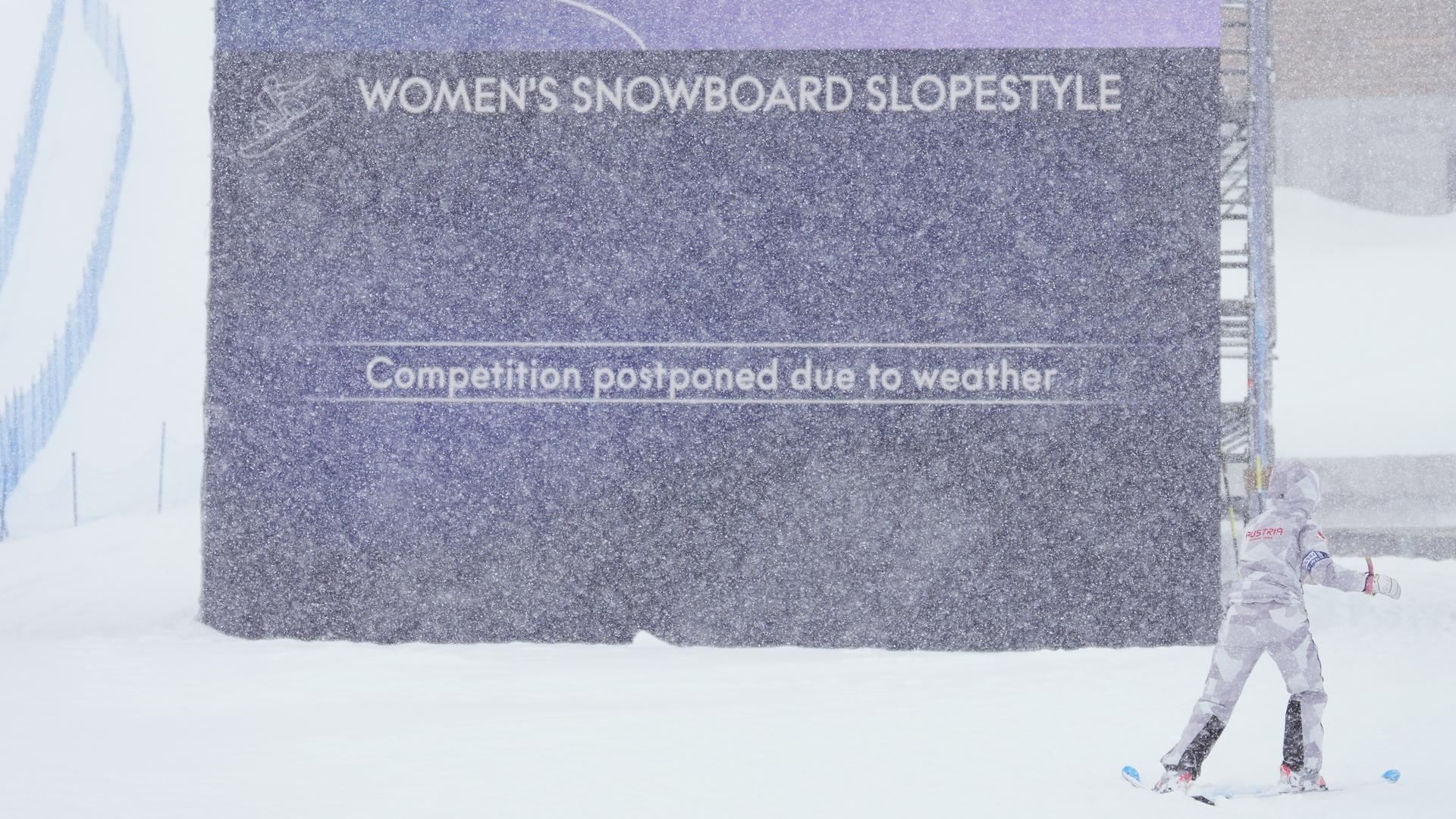 Inmitten dichten Schneefalls steht ein Schild mit der Aufschrift "Women's Snowboard Slopestyle - competiton postponed due to weather". 