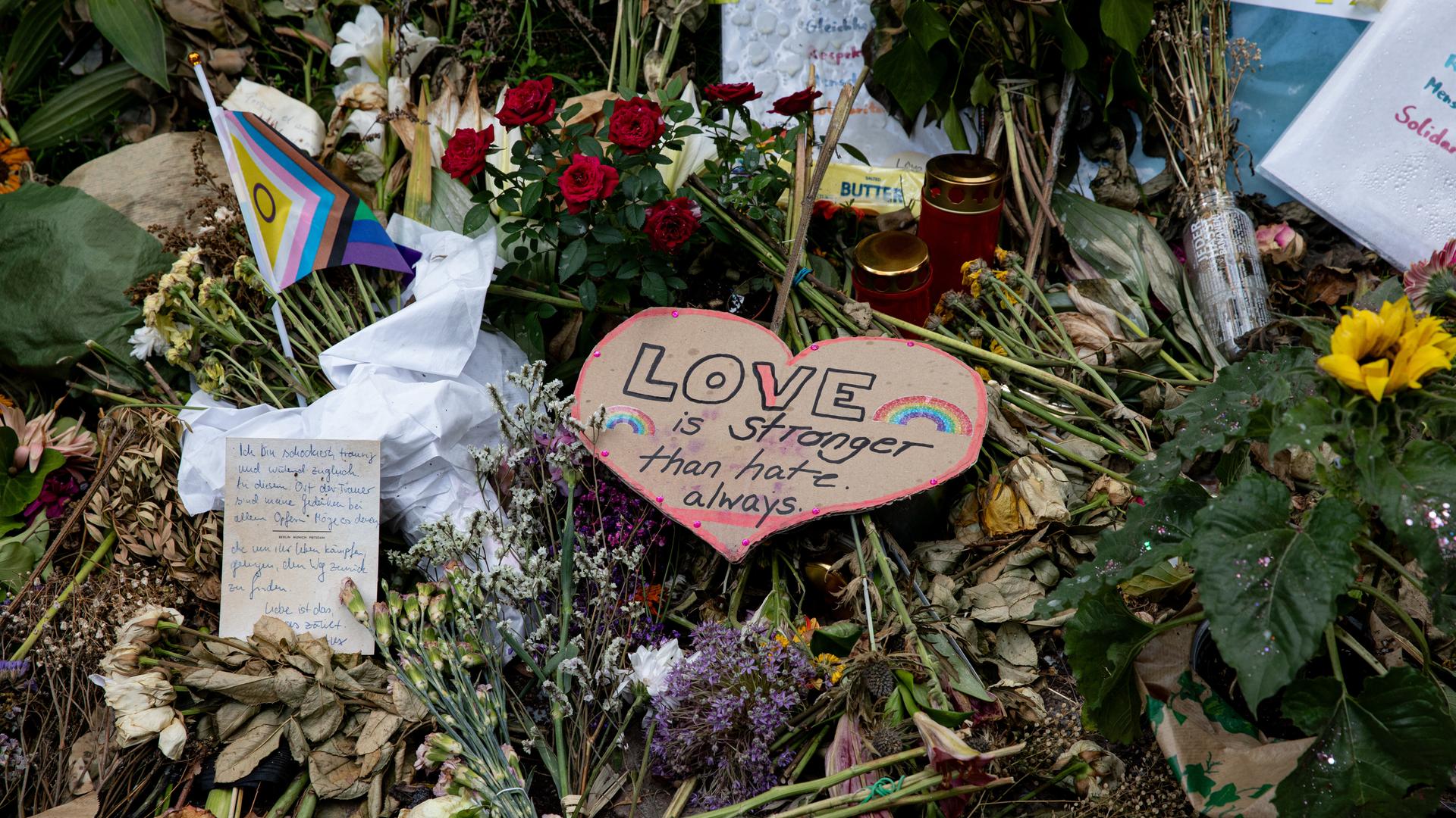 Nahaufnahme niedergelegter Blumen, Karten und LGBTIQ-Flaggen am Anschlagsort im Tiergarten.
